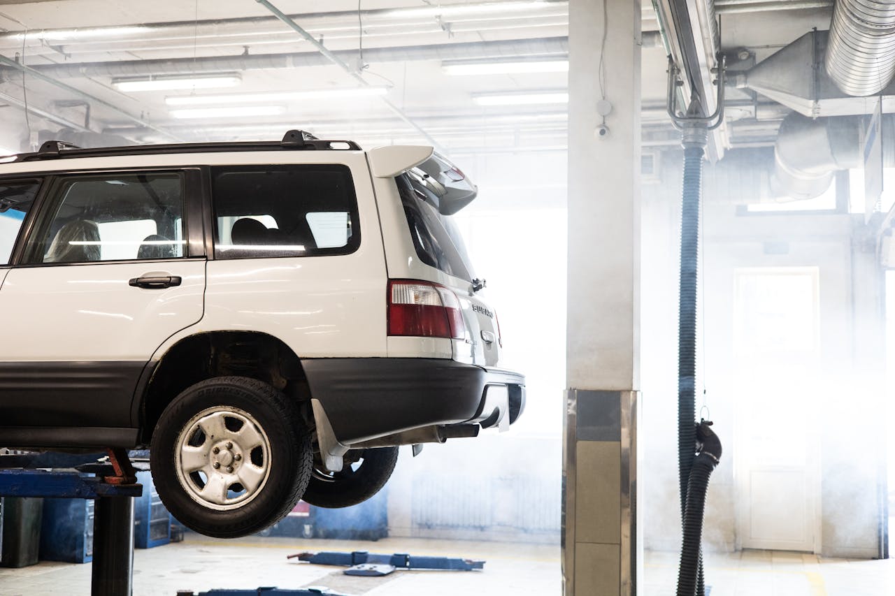 Services-01 A white SUV is elevated on a lift inside an auto repair shop for maintenance.